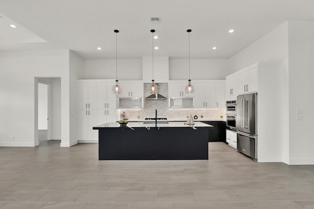 kitchen with wall chimney exhaust hood, hanging light fixtures, a center island with sink, high quality fridge, and white cabinetry