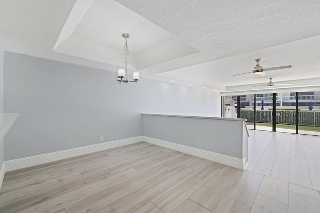 unfurnished room featuring a wall of windows, ceiling fan with notable chandelier, a tray ceiling, and a textured ceiling