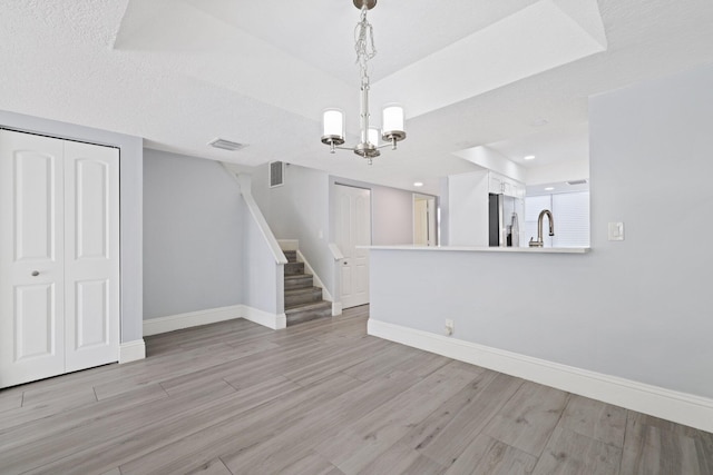 unfurnished room featuring a textured ceiling, light hardwood / wood-style floors, a tray ceiling, and an inviting chandelier