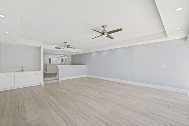 unfurnished room with light hardwood / wood-style floors, ceiling fan, sink, and a tray ceiling