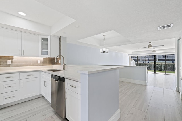 kitchen with backsplash, ceiling fan with notable chandelier, a raised ceiling, stainless steel dishwasher, and kitchen peninsula