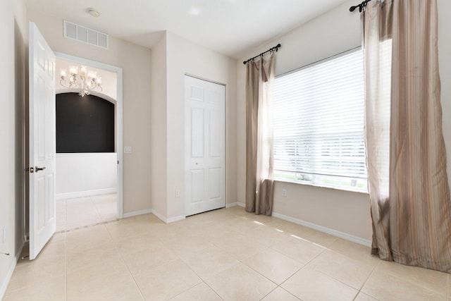 unfurnished bedroom with light tile patterned floors, baseboards, visible vents, and arched walkways