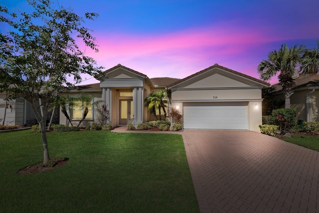 view of front of house featuring a garage, decorative driveway, a yard, and stucco siding