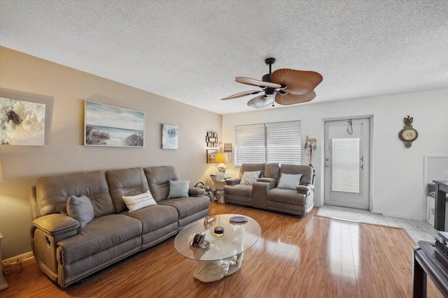 living room featuring light hardwood / wood-style flooring, ceiling fan, and a textured ceiling