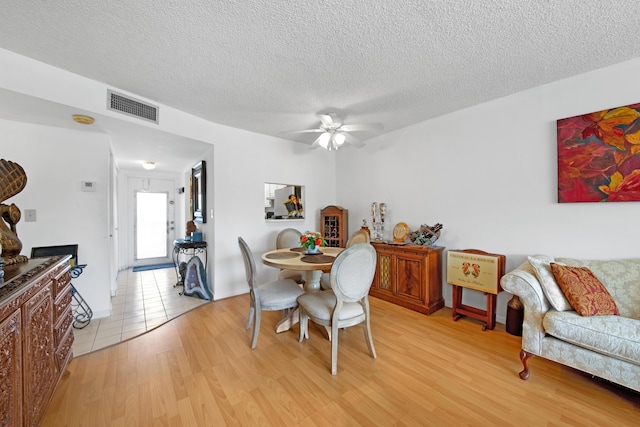 dining area with visible vents, ceiling fan, light wood-type flooring, and a textured ceiling