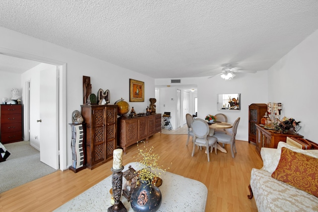 living room featuring visible vents, light wood-type flooring, a ceiling fan, and a textured ceiling