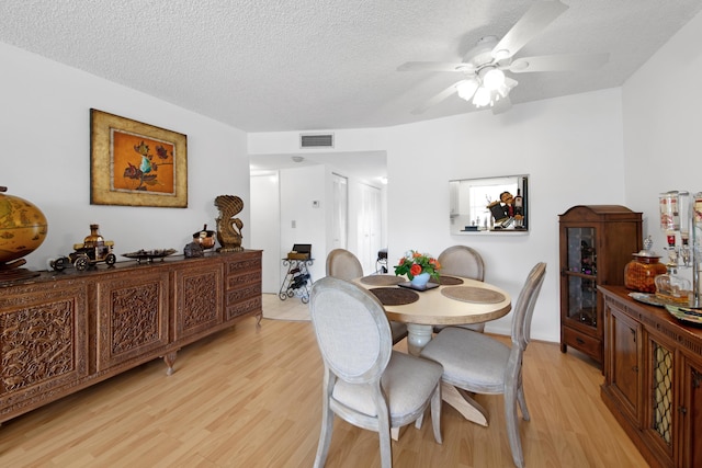 dining area featuring light wood finished floors, visible vents, a textured ceiling, and ceiling fan