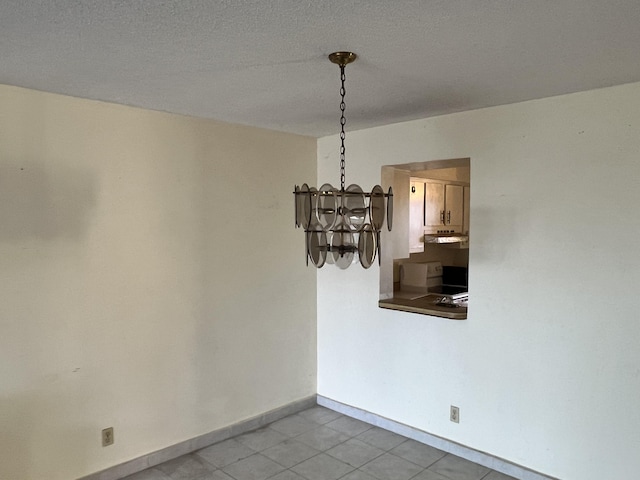 empty room featuring a notable chandelier, light tile floors, and a textured ceiling