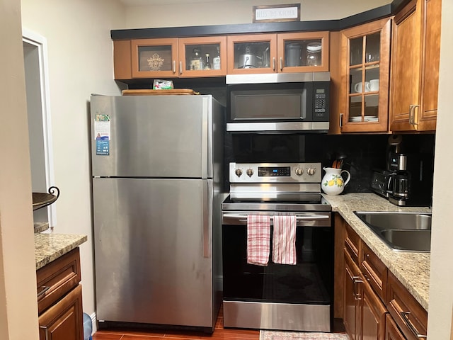 kitchen with appliances with stainless steel finishes, sink, light stone countertops, and backsplash