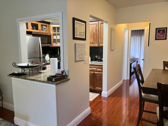 kitchen with dark hardwood / wood-style flooring, appliances with stainless steel finishes, tasteful backsplash, and dark stone counters