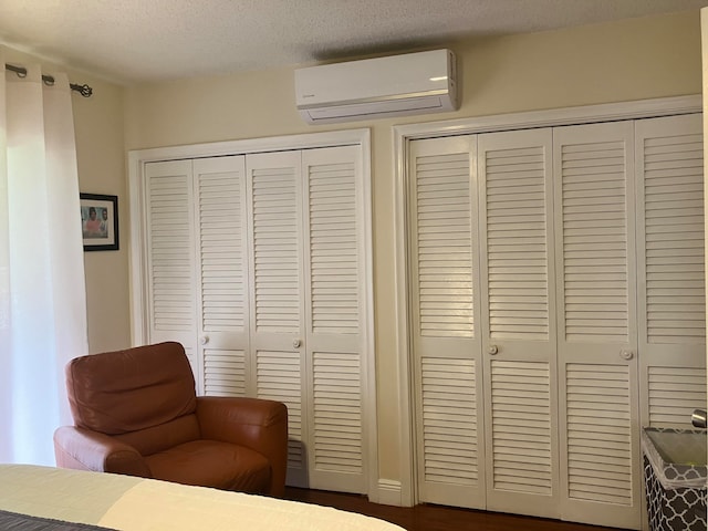 bedroom featuring two closets, a wall mounted air conditioner, and a textured ceiling