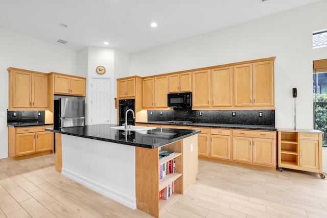 kitchen featuring light hardwood / wood-style floors, dark stone countertops, an island with sink, black appliances, and sink