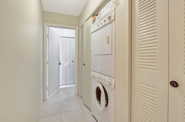 clothes washing area with a textured ceiling, light tile floors, and stacked washer / drying machine