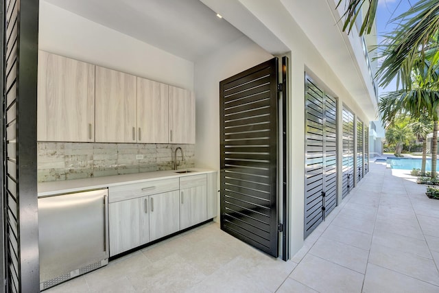 bar with light brown cabinetry, sink, tasteful backsplash, light tile patterned floors, and stainless steel built in fridge