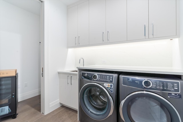 laundry area featuring sink, washer and clothes dryer, cabinets, beverage cooler, and light wood-type flooring