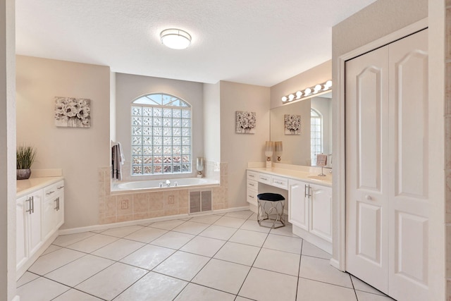 bathroom with tile flooring, tiled tub, vanity, and a textured ceiling