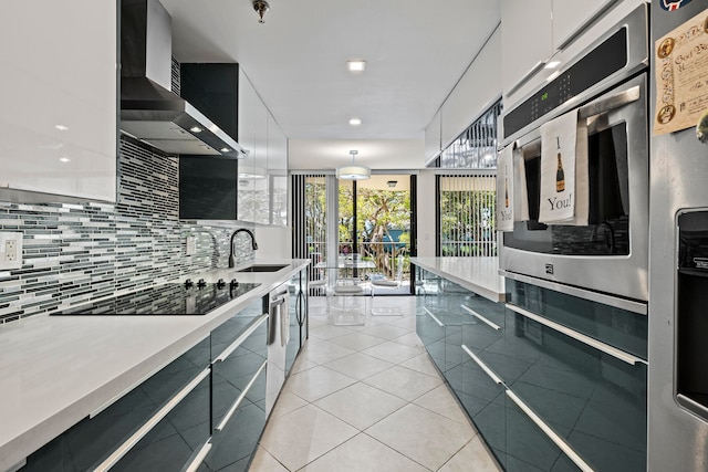 kitchen with hanging light fixtures, wall chimney range hood, stainless steel appliances, sink, and tasteful backsplash