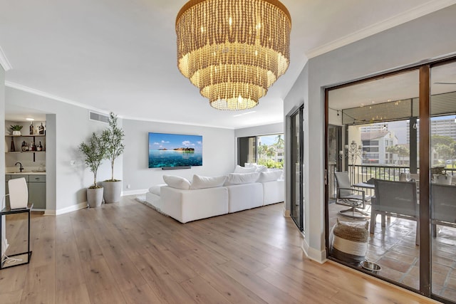 living room featuring hardwood / wood-style flooring, crown molding, sink, and a notable chandelier