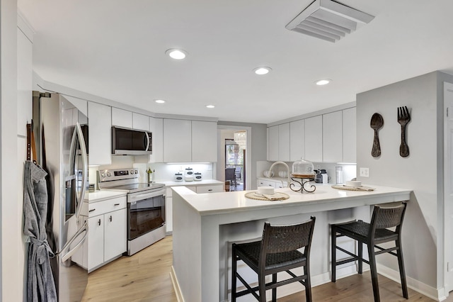 kitchen featuring appliances with stainless steel finishes, kitchen peninsula, light wood-type flooring, and a breakfast bar area