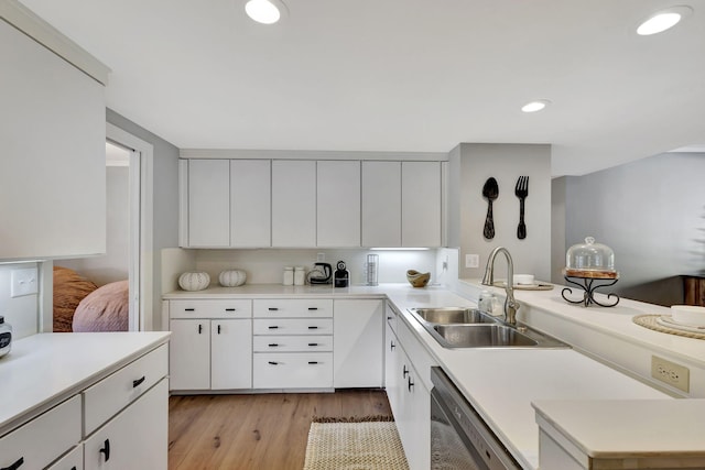 kitchen with sink, light hardwood / wood-style floors, dishwashing machine, and white cabinetry