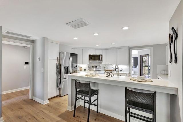 kitchen with appliances with stainless steel finishes, a breakfast bar, sink, white cabinetry, and light hardwood / wood-style flooring