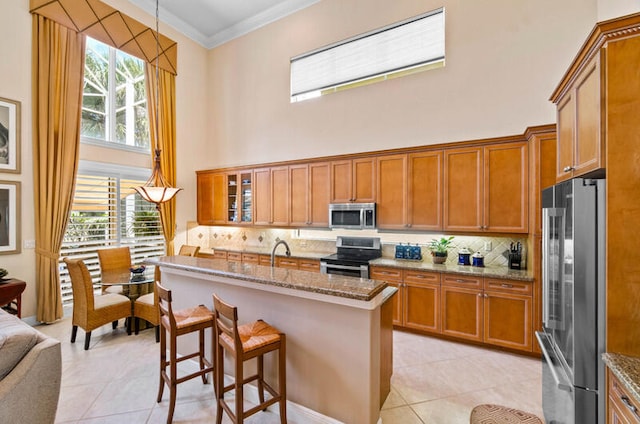 kitchen with light tile floors, backsplash, a high ceiling, stainless steel appliances, and a center island with sink