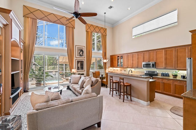 living room featuring a high ceiling, crown molding, ceiling fan, and light tile floors