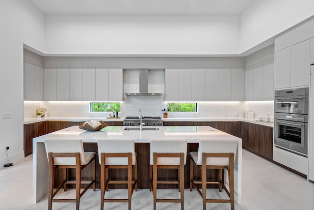 kitchen featuring a breakfast bar area, a kitchen island with sink, and wall chimney range hood