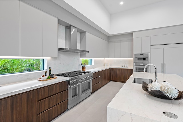 kitchen with sink, high end appliances, backsplash, wall chimney range hood, and white cabinetry