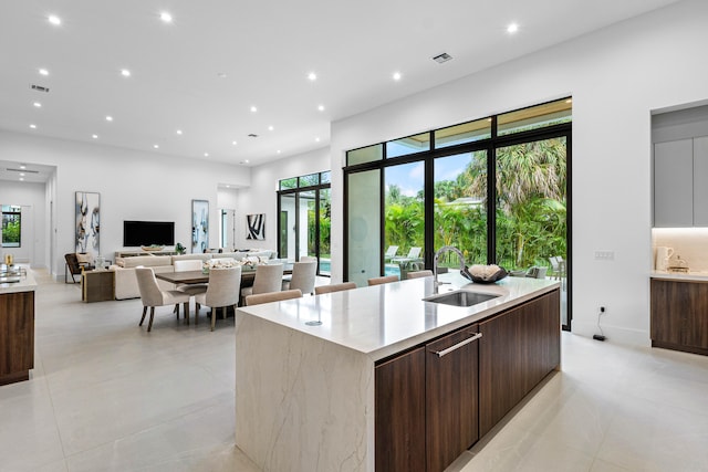 kitchen with a center island with sink, dark brown cabinets, sink, and light tile patterned floors