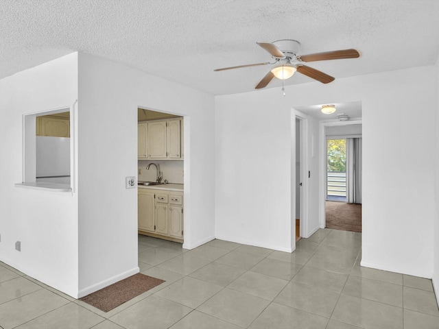 empty room with sink, ceiling fan, light tile floors, and a textured ceiling