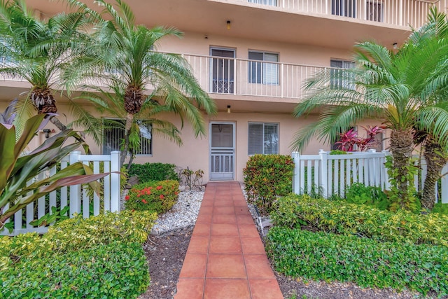 property entrance featuring stucco siding, fence, and a balcony