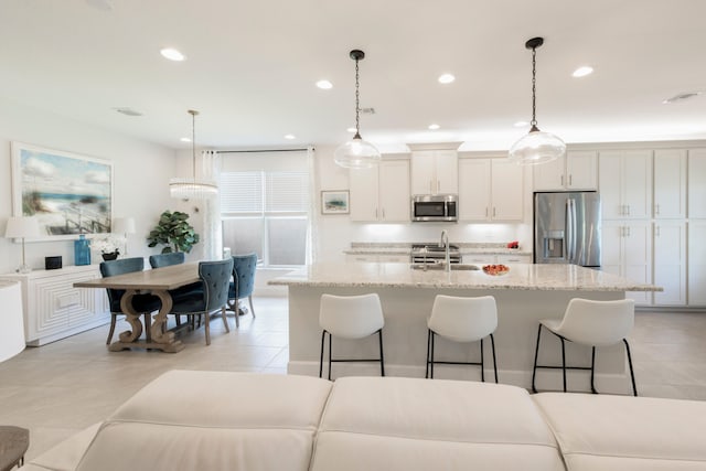 kitchen with a kitchen island with sink, stainless steel appliances, light tile floors, and decorative light fixtures