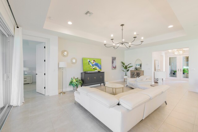 living room with french doors, a notable chandelier, light tile floors, and a tray ceiling