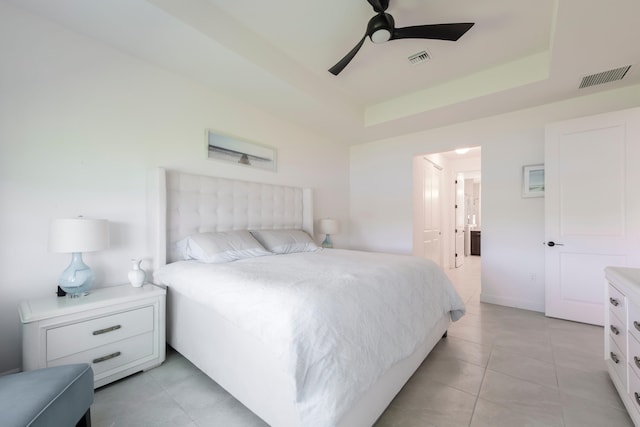 bedroom with ceiling fan, a tray ceiling, and light tile floors