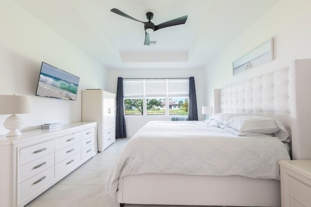 bedroom with ceiling fan, light tile floors, and a tray ceiling