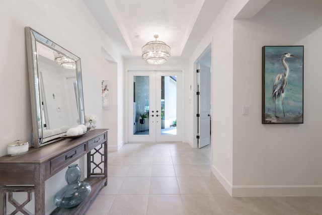 foyer entrance featuring french doors, light tile floors, a tray ceiling, and an inviting chandelier