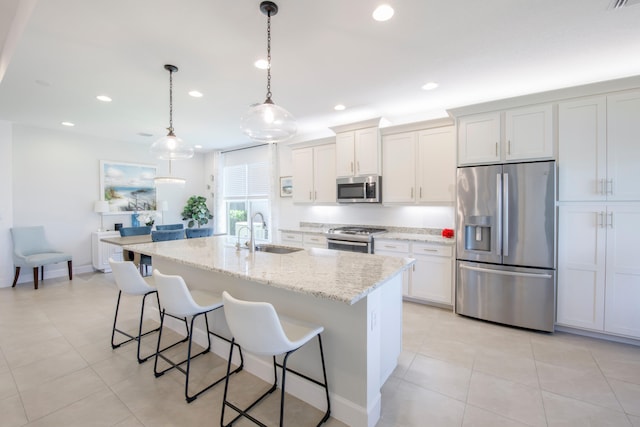 kitchen with appliances with stainless steel finishes, light tile floors, a breakfast bar, a center island with sink, and pendant lighting