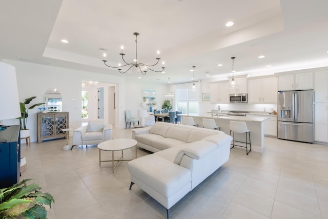 tiled living room with a wealth of natural light, a chandelier, and a tray ceiling