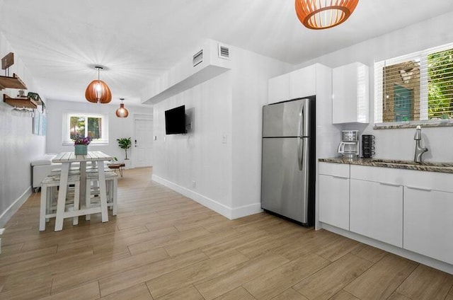 kitchen with sink, stainless steel refrigerator, white cabinetry, hanging light fixtures, and plenty of natural light