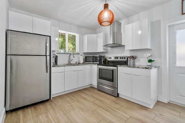 kitchen with appliances with stainless steel finishes, white cabinets, and wall chimney exhaust hood