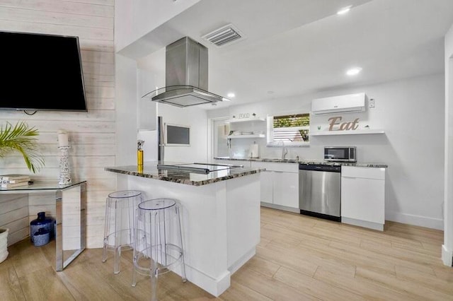 kitchen with stainless steel appliances, light hardwood / wood-style floors, dark stone countertops, white cabinets, and island exhaust hood