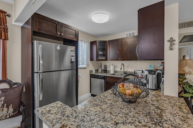 kitchen featuring stainless steel appliances, dark brown cabinetry, sink, and light stone counters