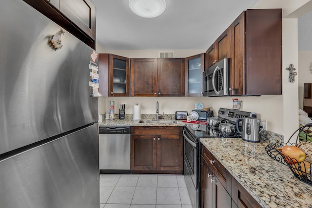 kitchen featuring dark brown cabinetry, light stone counters, light tile floors, sink, and stainless steel appliances