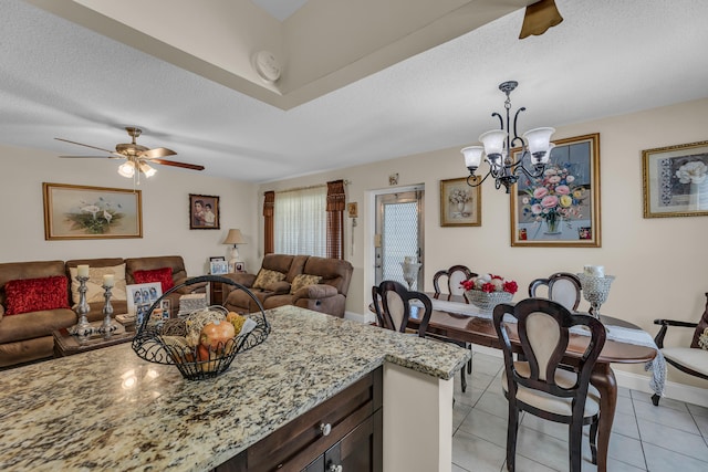 kitchen with hanging light fixtures, ceiling fan with notable chandelier, light tile floors, light stone counters, and a textured ceiling