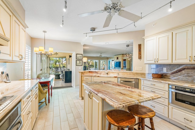 kitchen with ceiling fan with notable chandelier, kitchen peninsula, stainless steel appliances, sink, and track lighting