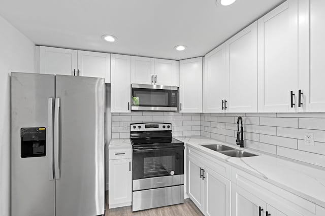 kitchen with sink, light wood-type flooring, white cabinetry, stainless steel appliances, and light stone countertops