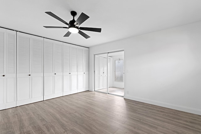 unfurnished bedroom featuring wood-type flooring, ceiling fan, and two closets