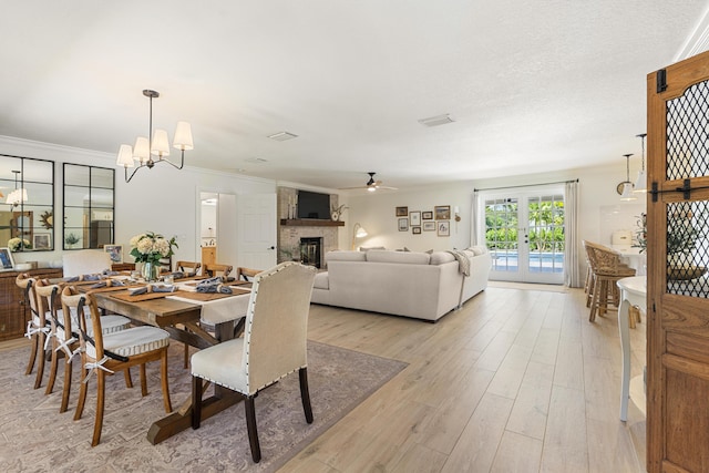 dining room featuring a large fireplace, light hardwood / wood-style flooring, ornamental molding, french doors, and ceiling fan with notable chandelier