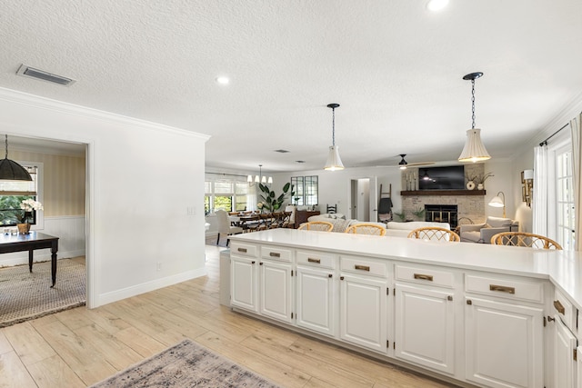 kitchen featuring white cabinets, light hardwood / wood-style flooring, crown molding, and a fireplace